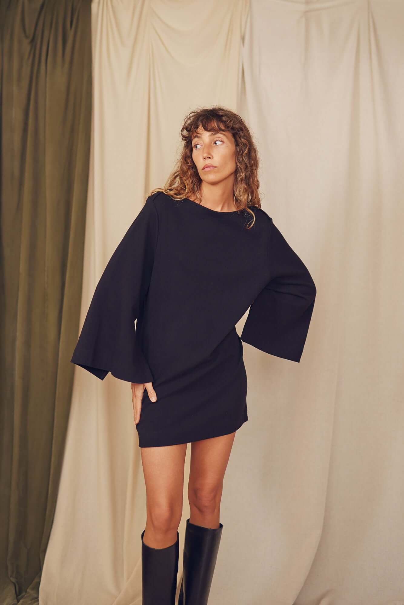 Model wearing a black mini dress with flared sleeves, highlighting its minimalist design and eco-friendly fabric.