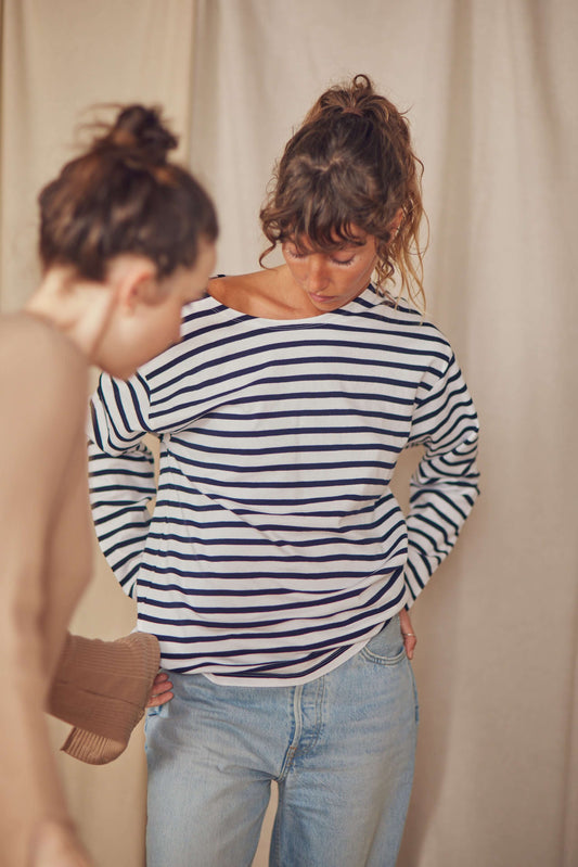 Model wearing a classic Breton sweatshirt in white and navy stripes, featuring a wide neckline and paired with jeans.