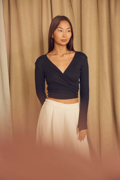Model wearing a Black Wool Wrap Top with thumb holes, styled with a flowing skirt, showcasing its elegant design.