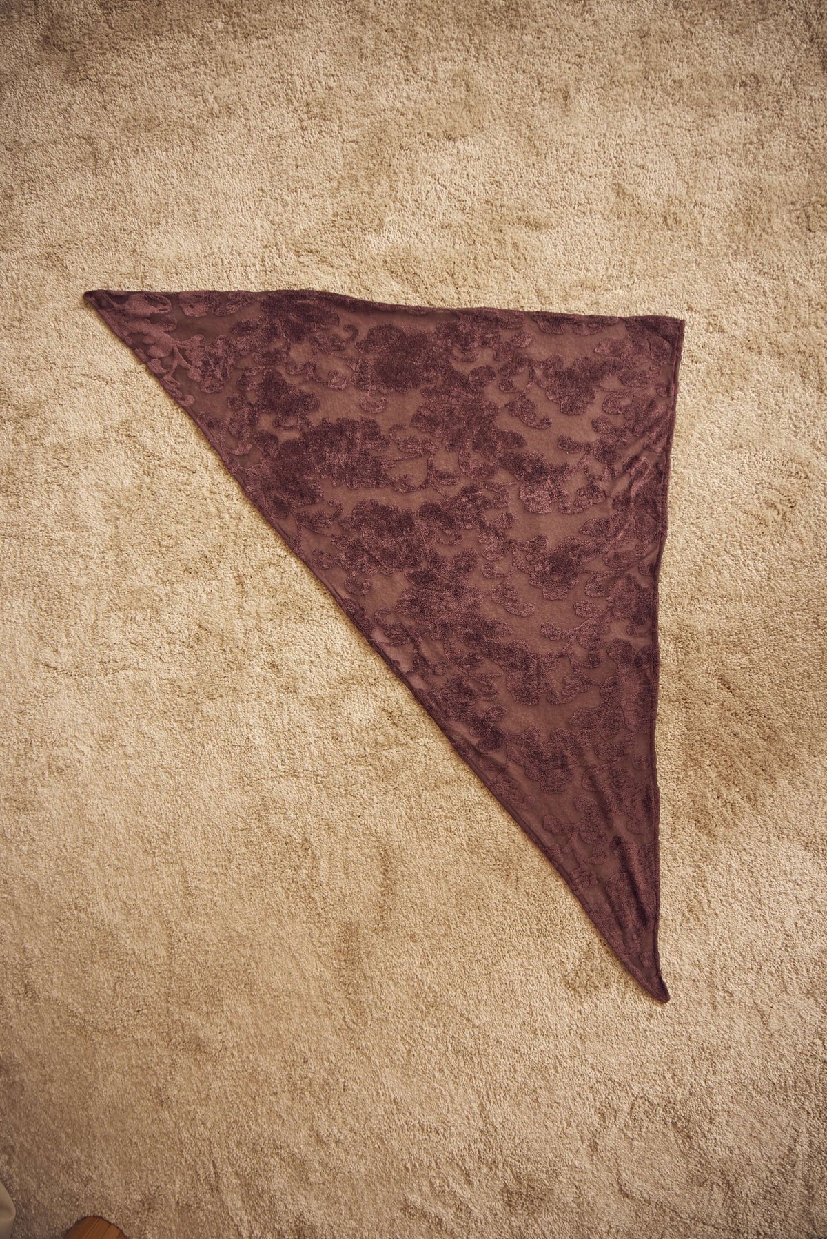Cocoa Devoré Triangle Scarf displayed on a textured surface, showcasing its intricate devoré pattern and triangular shape.
