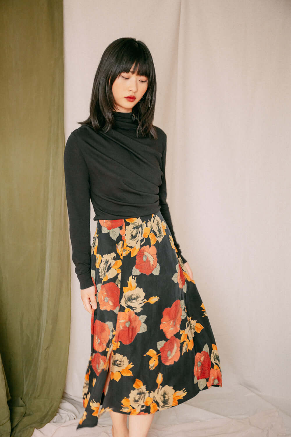 Woman wearing black drape knit top with floral skirt, showcasing feminine bust detail, ideal for layering, in an exclusive online piece.