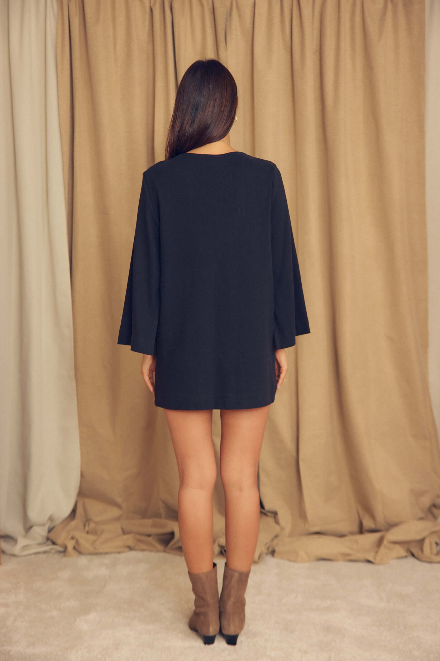 Back view of a model wearing a Black Organic Cotton Mini Dress with Flared Sleeves, showcasing the flared sleeves and mini length.