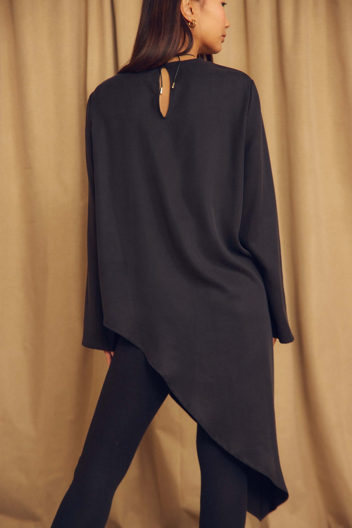 Rear view of a model wearing the Black Lyocell Asymmetric Tunic showcasing its unique hemline and sleek design.