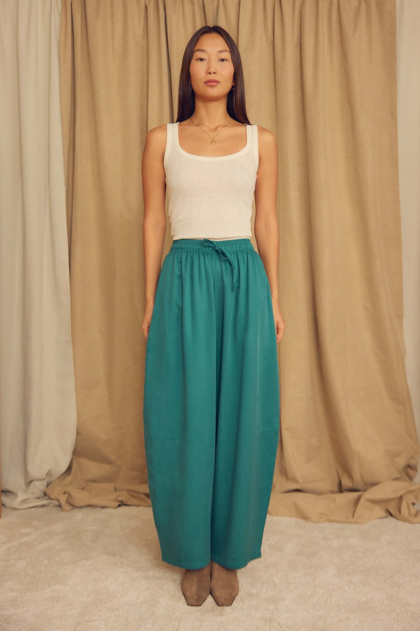 Model wearing Teal Lyocell Barrel-Leg Trousers with a relaxed fit and elasticated waist.