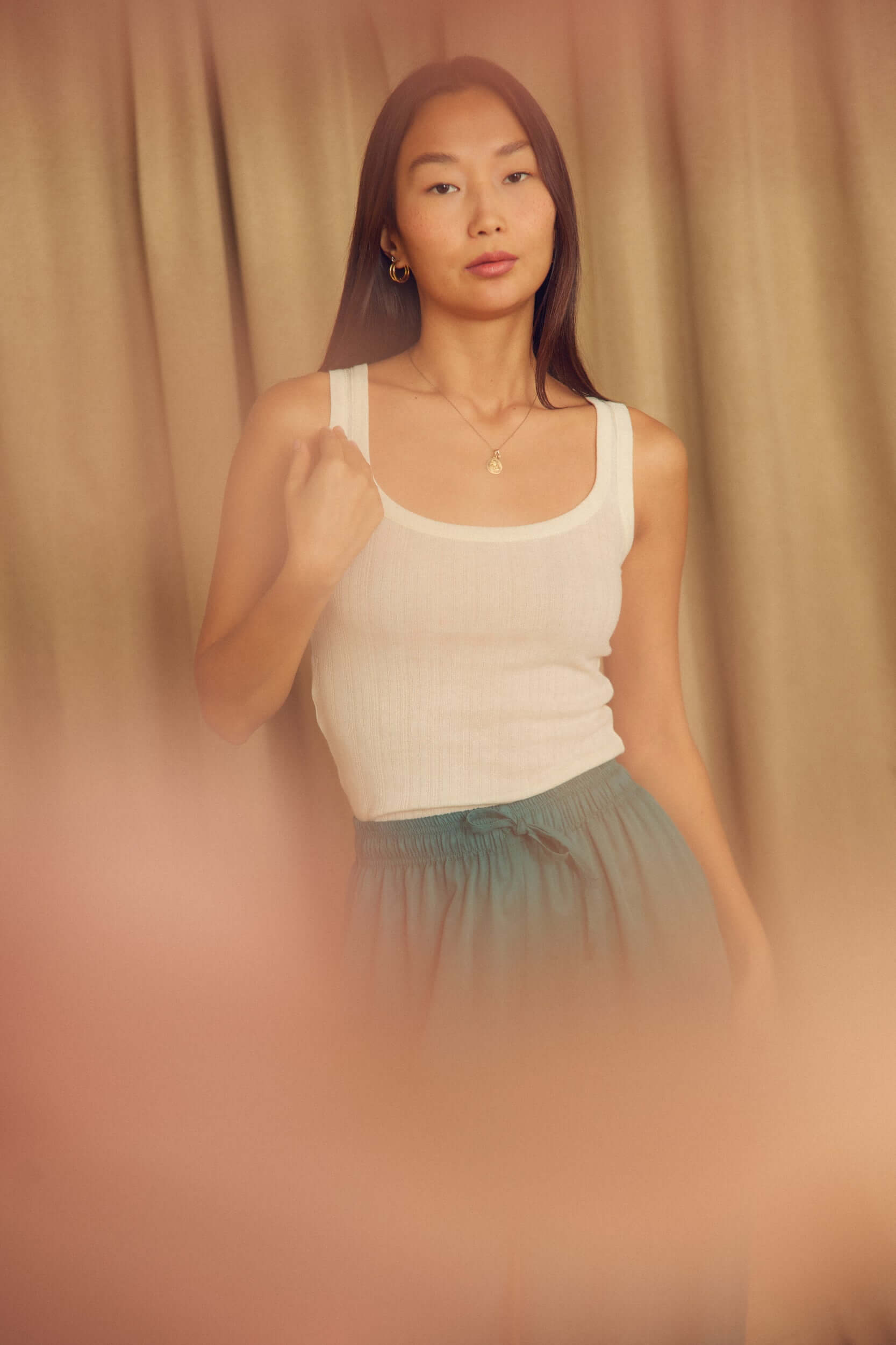 Model wearing Ecru Lyocell Ribbed Tank Top with a green skirt in a softly lit room.