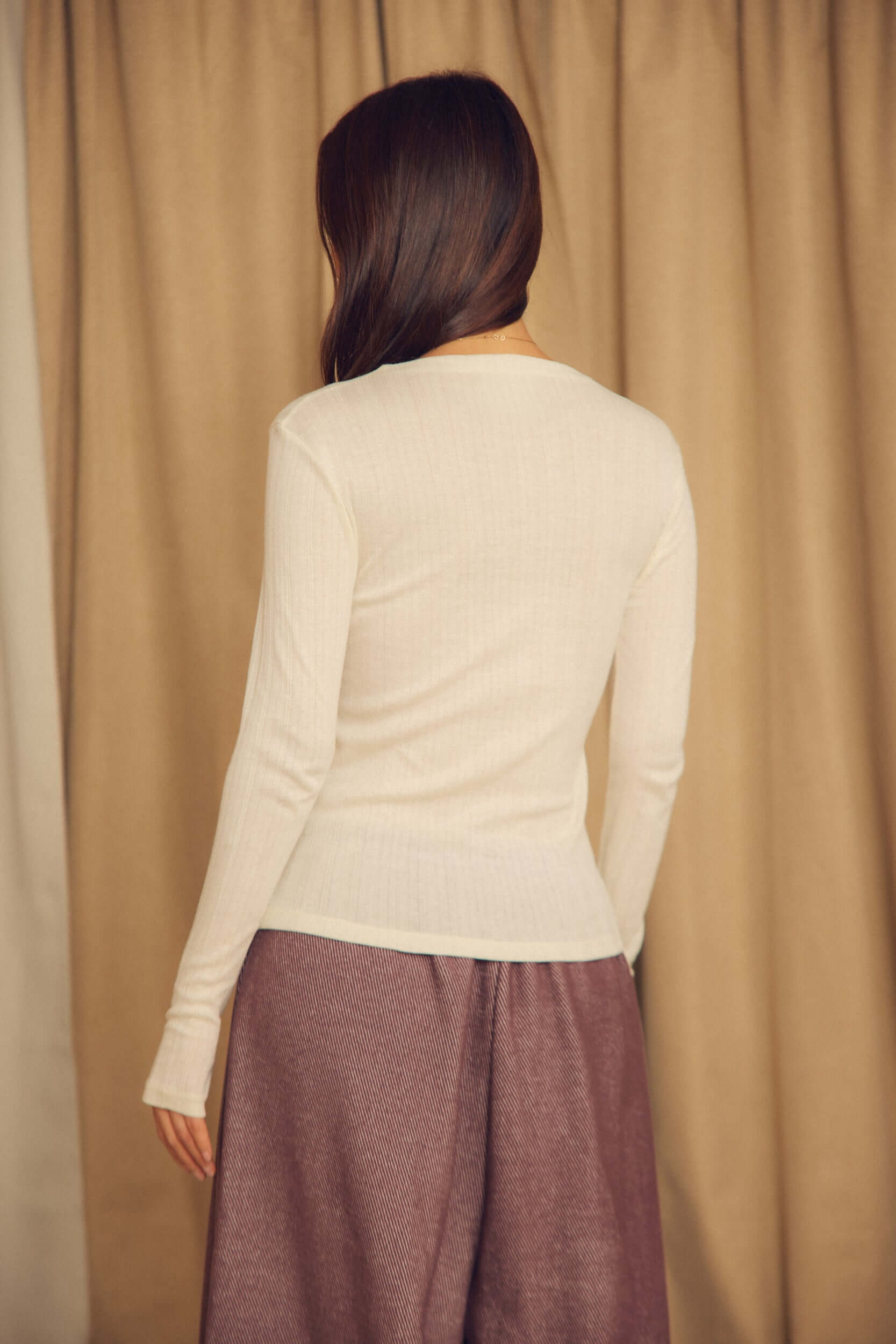 Back view of a model wearing the Ecru Lyocell Ribbed Long Sleeve Top paired with a long skirt.