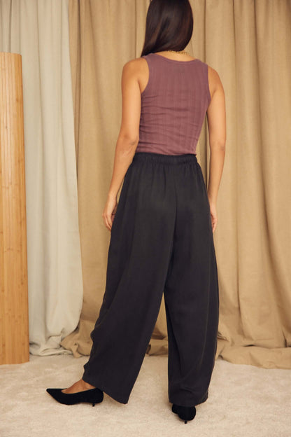 Back view of a woman wearing Black Lyocell Barrel-Leg Trousers with a fitted top in a stylish interior.