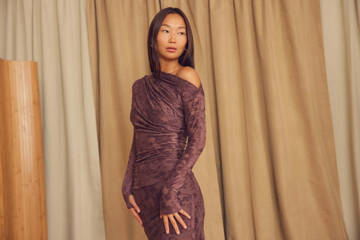 Model wearing a Cocoa Devoré Drape Top in a cozy interior setting, showcasing abstract pattern and fluid draping.