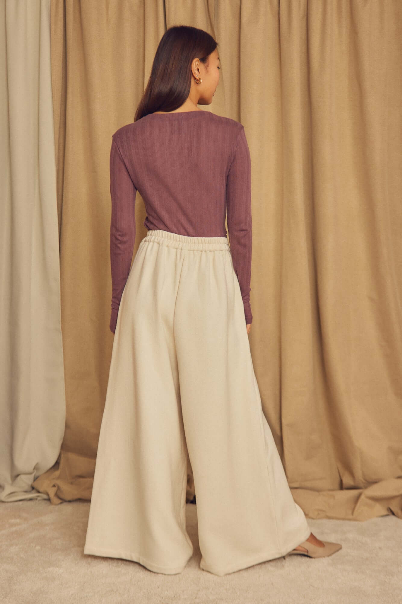 Ecru Organic Cotton Wide Trousers showcased on a model from the back with a purple top and a neutral background.