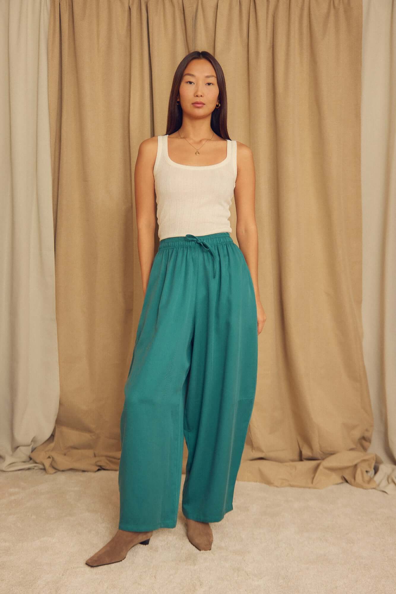Model wearing Teal Lyocell Barrel-Leg Trousers with a white tank top in a neutral setting.