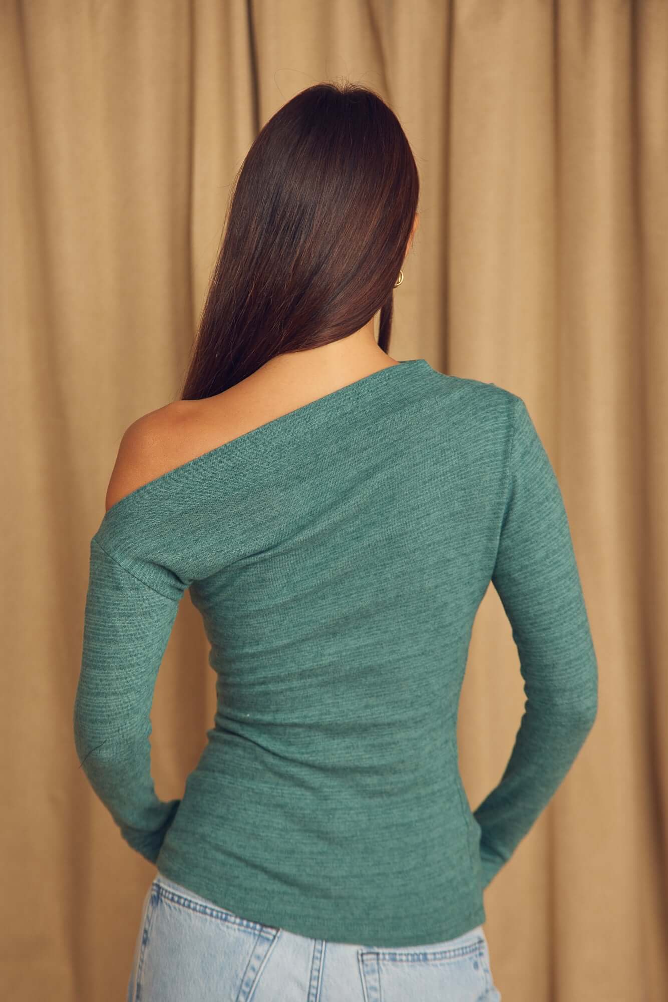 Back view of a woman wearing a Teal Wool Drape Top with thumb holes against a soft fabric background.