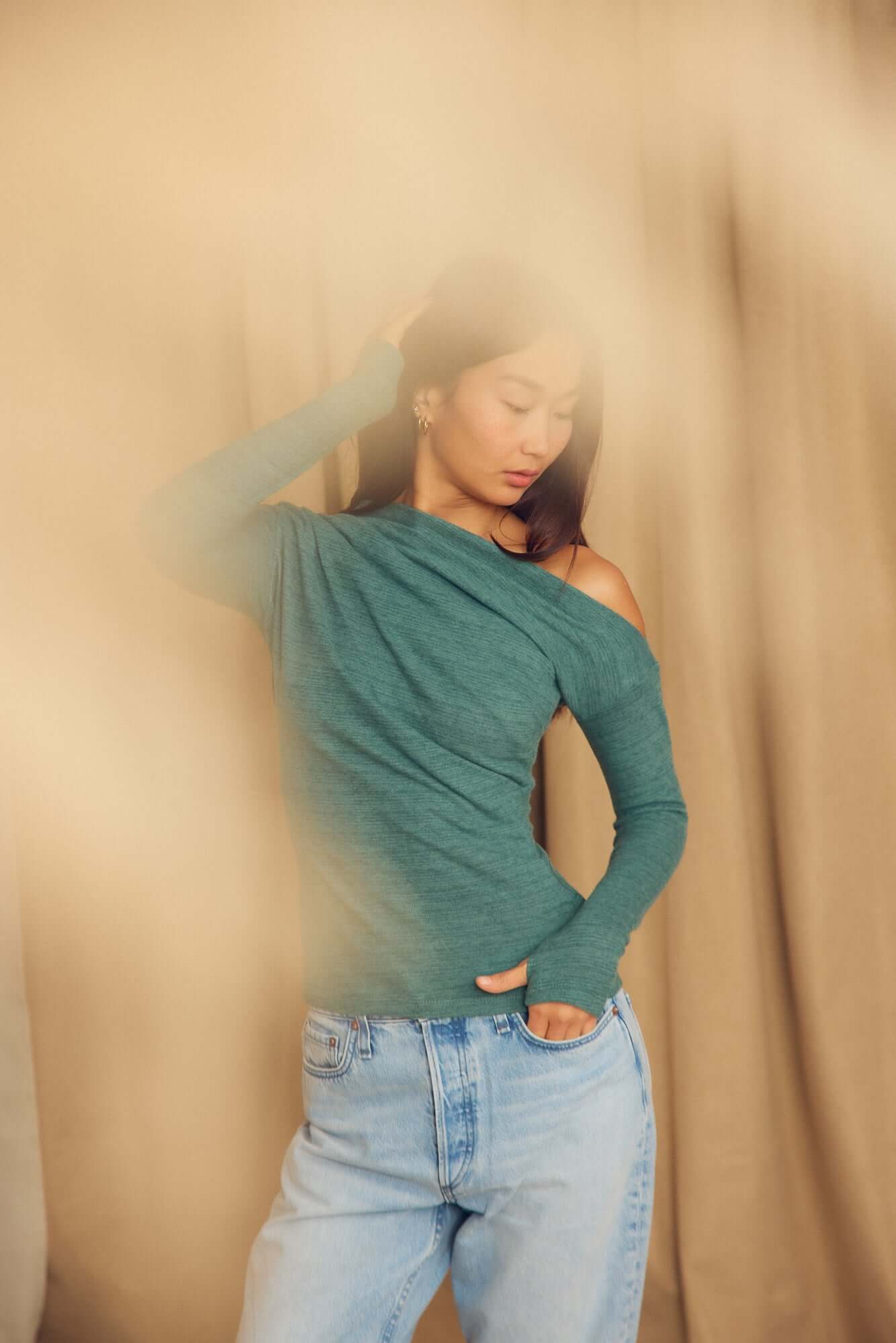 Model wearing a Teal Wool Drape Top with thumb holes, styled with casual jeans, showcasing its elegant draped neckline.
