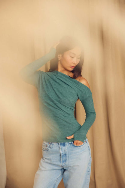 Model wearing a Teal Wool Drape Top with thumb holes, styled with casual jeans, showcasing its elegant draped neckline.