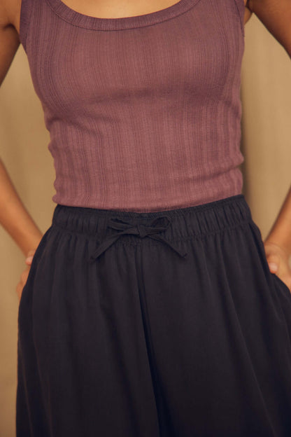 Close-up of a model wearing a purple tank top with Black Lyocell Barrel-Leg Trousers featuring an elasticated waist.
