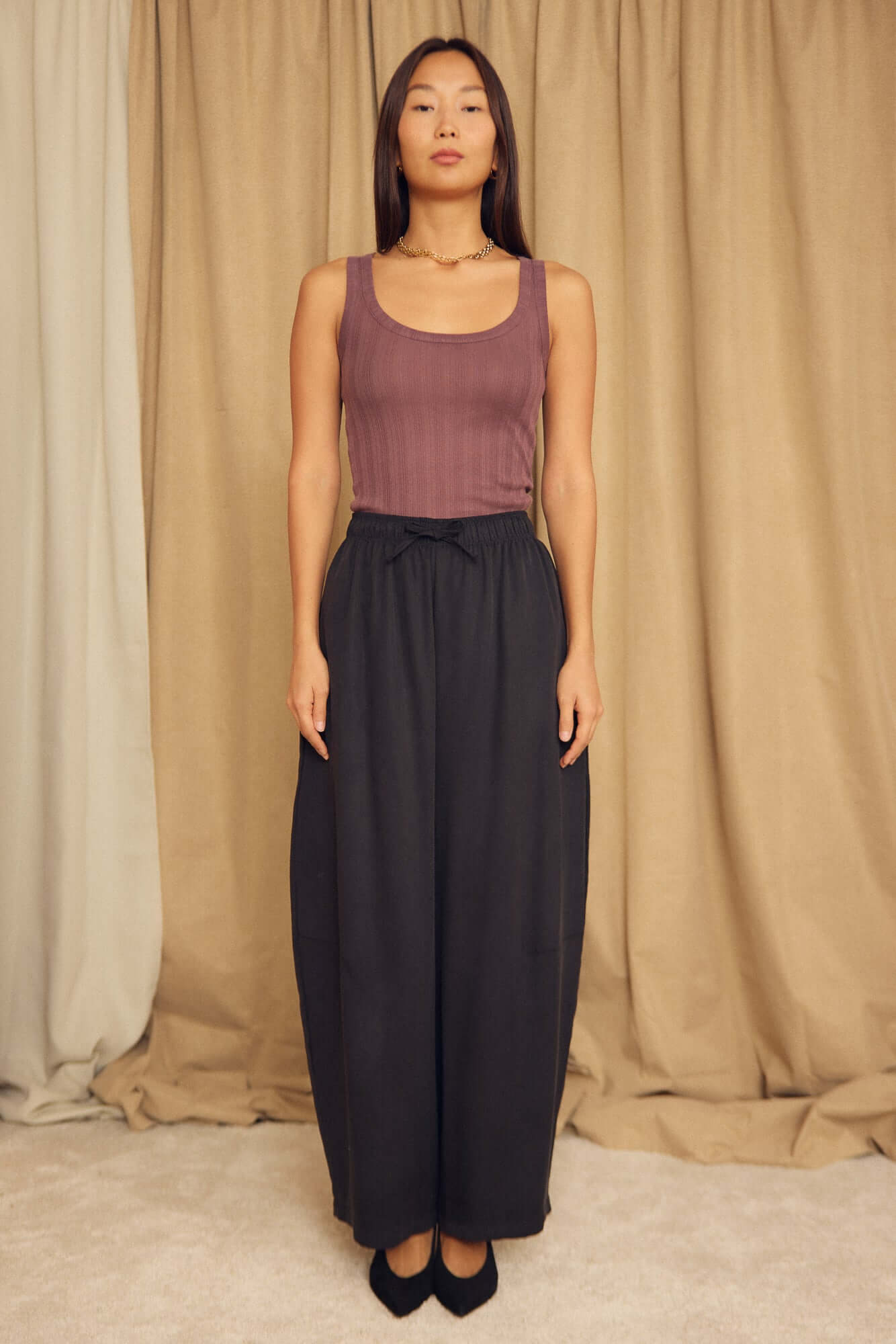 Model wearing a Cocoa Lyocell Ribbed Tank Top in cocoa brown paired with black wide-leg pants.