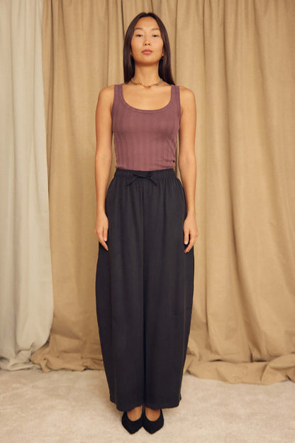 Model wearing a Cocoa Lyocell Ribbed Tank Top in cocoa brown paired with black wide-leg pants.
