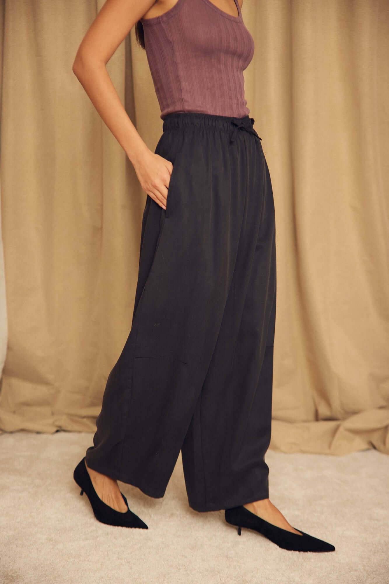 Model wearing Black Lyocell Barrel-Leg Trousers with elasticated waist and relaxed silhouette.