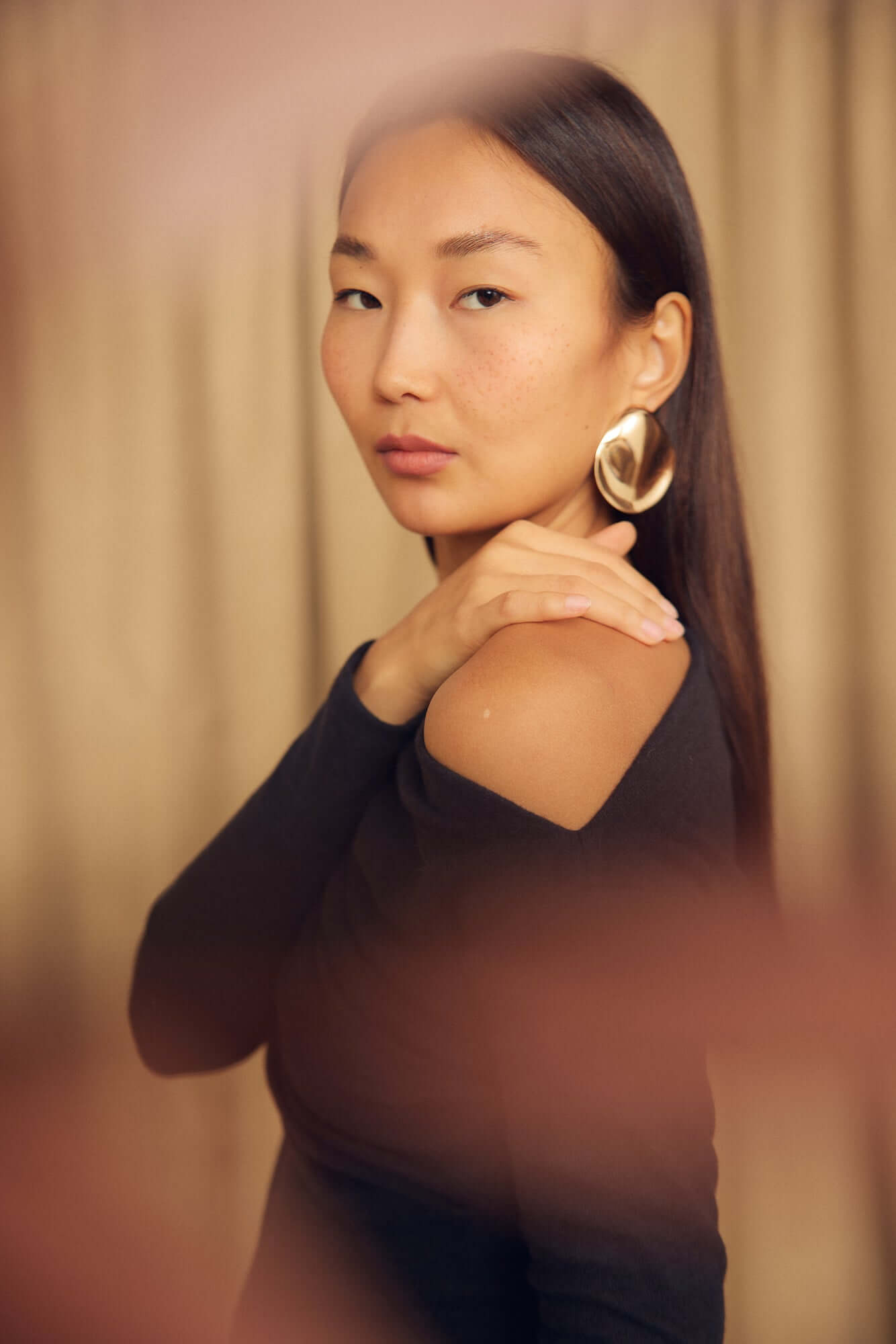 Model wearing a Black Wool Drape Top with an elegant draped neckline and gold hoop earrings.