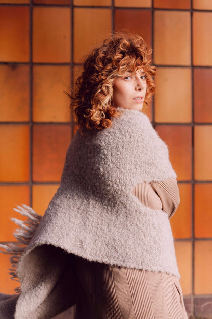 Woman wearing a versatile grey poncho scarf made from sustainable materials, against a warm-toned background.