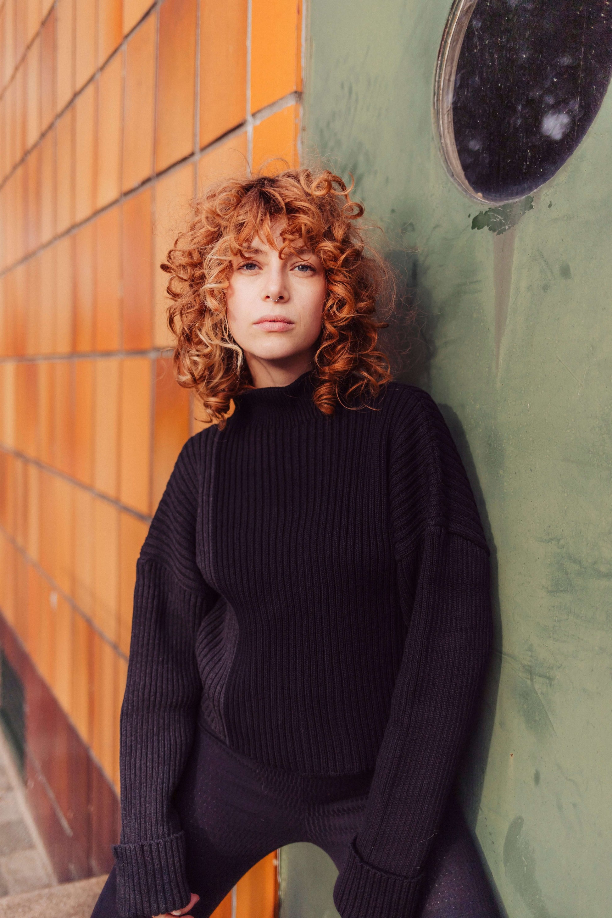 Model wearing a bicolor black sweater made from organic cotton with high neck, set against a modern urban backdrop.