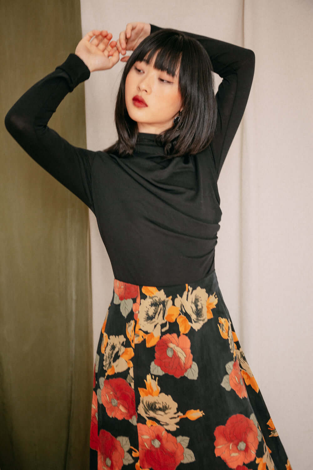 Woman wearing black drape knit top and floral skirt, showcasing drape bust detail.