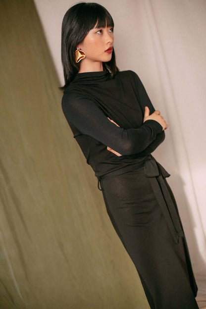 Woman wearing black drape knit dress with drape bust detail, standing with arms crossed.