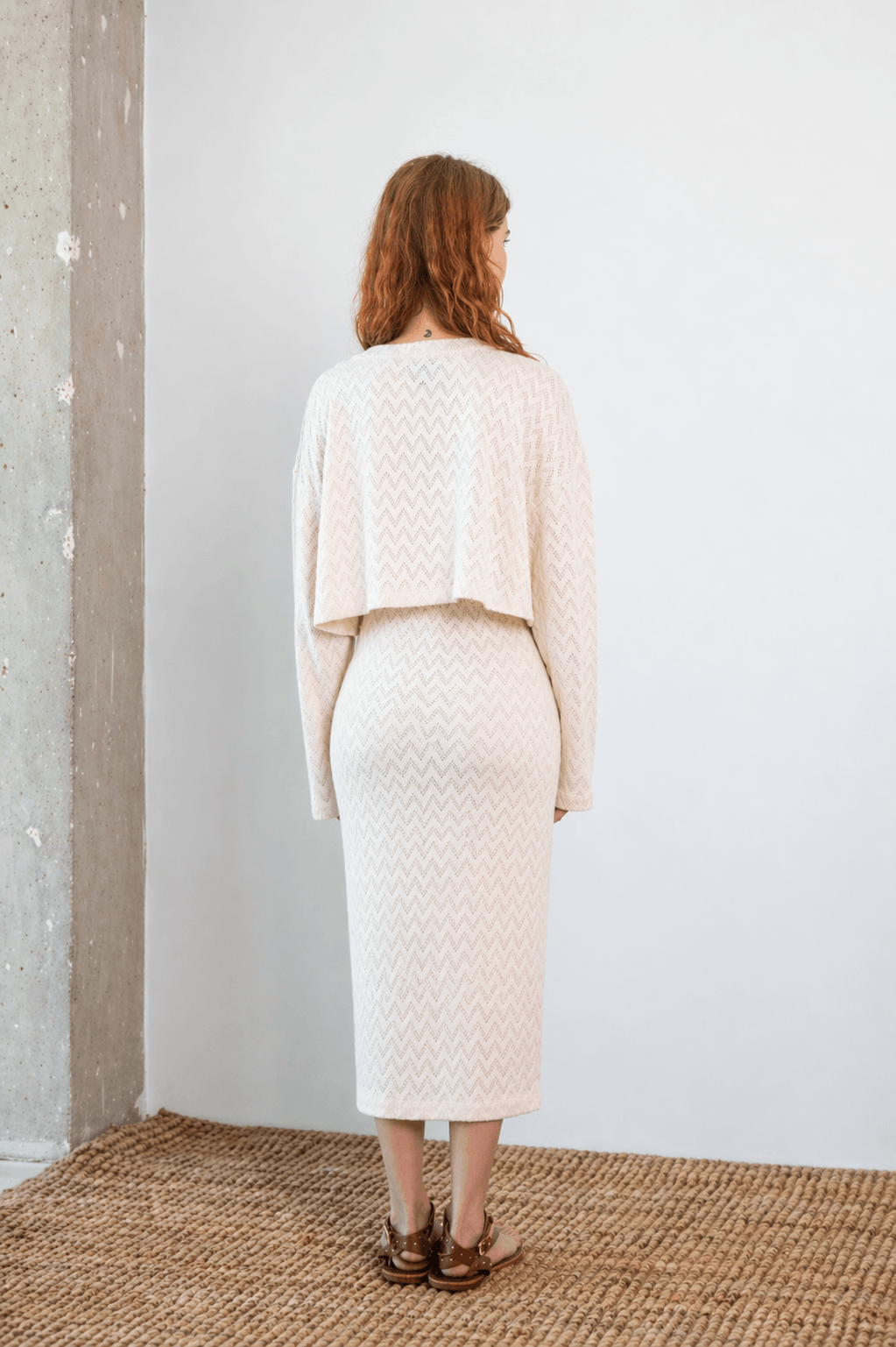 Woman wearing Crochet Organic Cotton Long Sleeve Top, seen from the back in an ecru color, showcasing its cropped design.