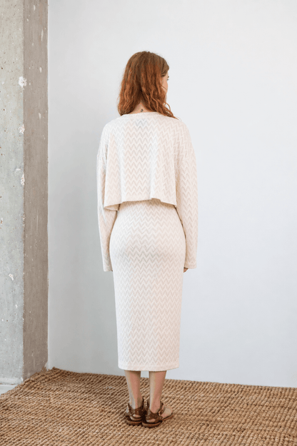 Woman wearing Crochet Organic Cotton Long Sleeve Top, seen from the back in an ecru color, showcasing its cropped design.