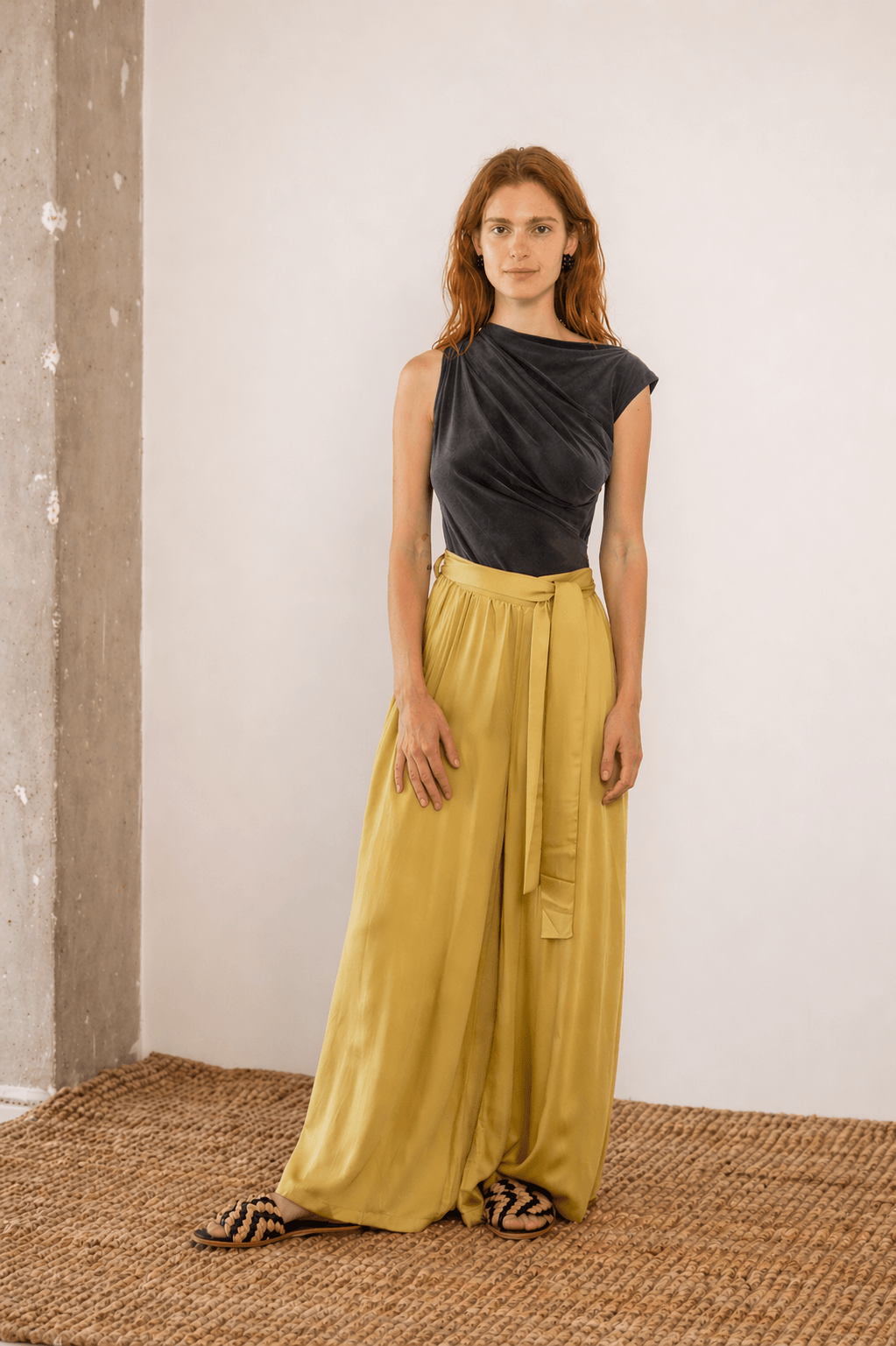 Drape Neckline Bodysuit in Slate Black paired with yellow flowy trousers, showcasing modern styling in a minimalist setting.