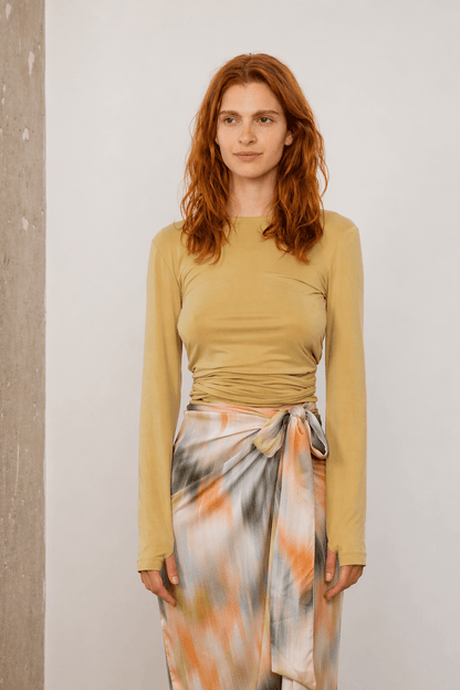 Cupro Multiway Wrap Top in Soft Olive, worn by a model styled with a colorful skirt.