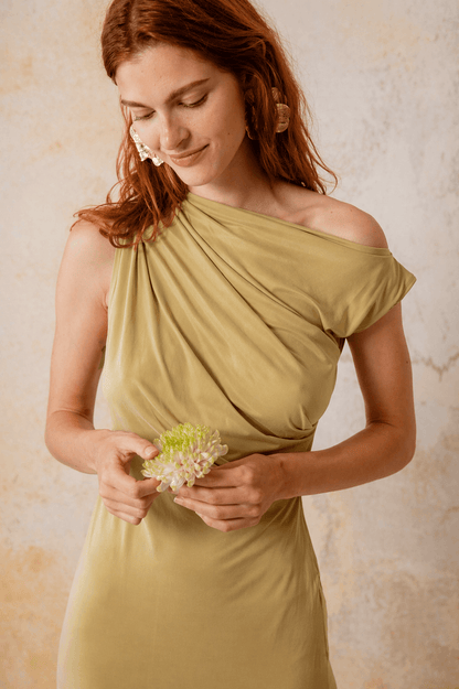 Drape Cupro Midi Dress in Olive worn by a model holding a flower, showcasing the dress's elegant design and draped neckline.