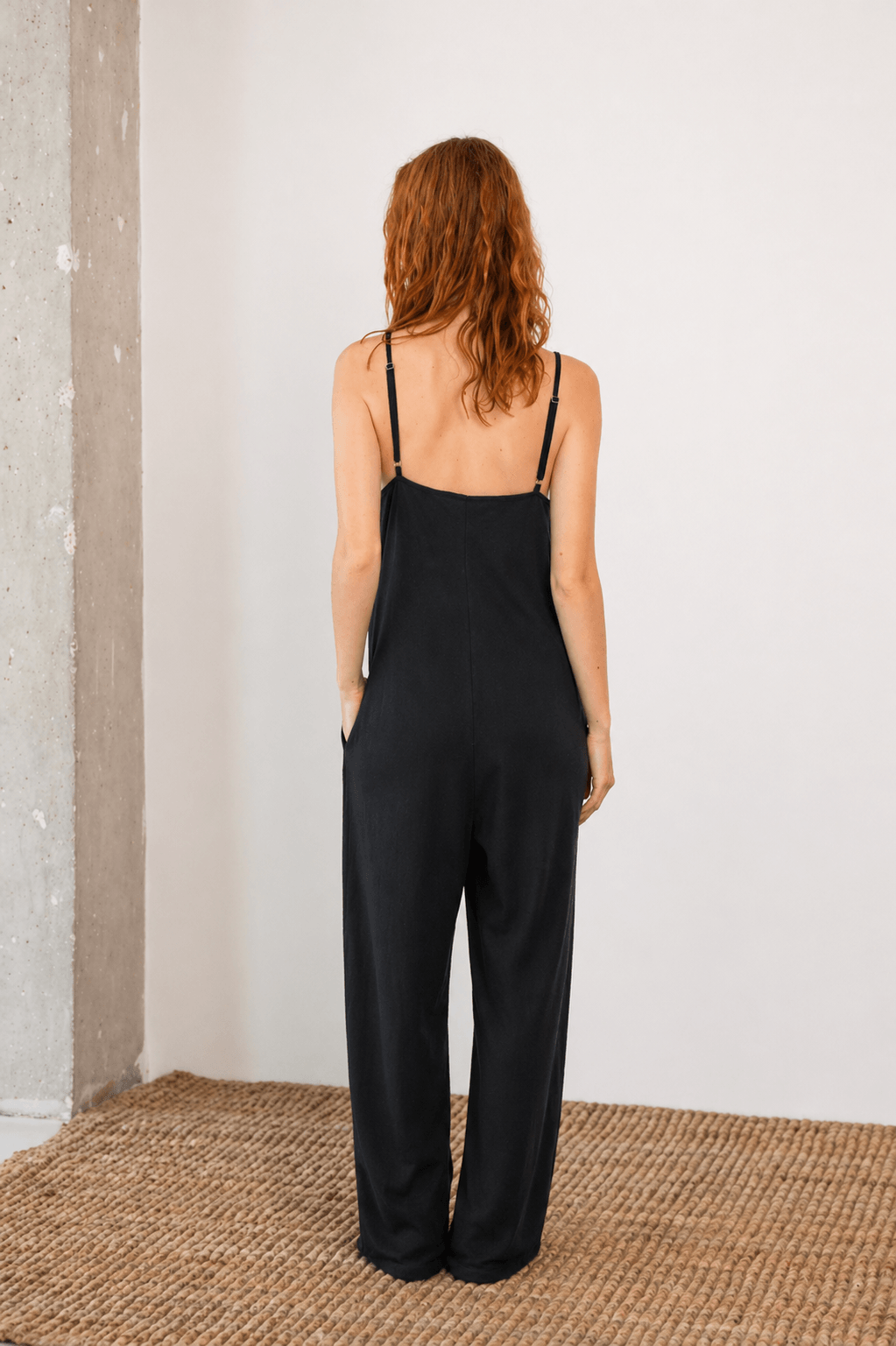 Model wearing Organic Cotton Wide Jumpsuit in Black, showcasing the back view and relaxed silhouette.