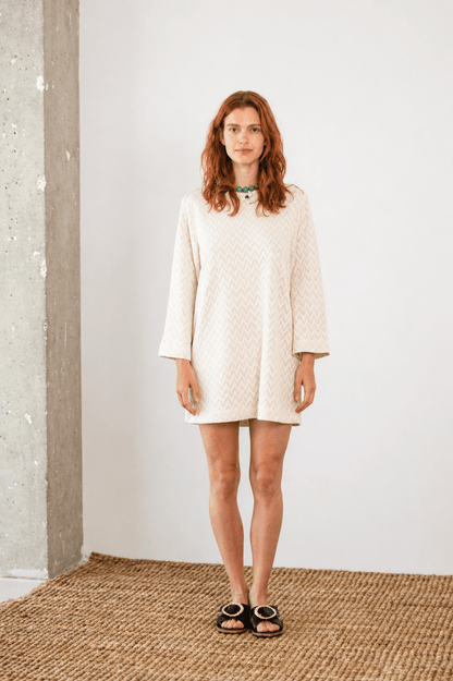Model wearing an Organic Cotton Crochet Mini Dress with flared sleeves in ecru, set against a neutral backdrop.