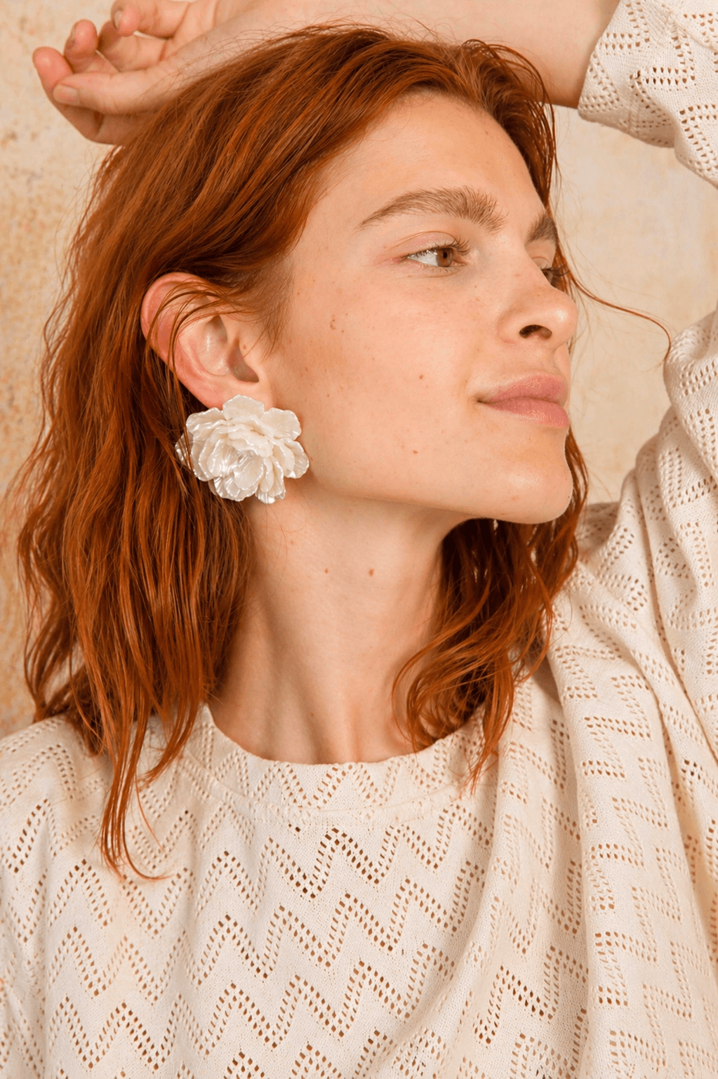 Woman wearing a textured white top with a floral earring, showcasing a casual yet stylish look.