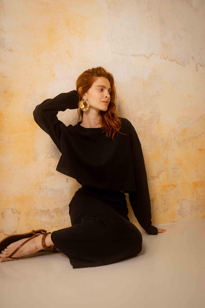 Organic Cotton Long Sleeve Top in Black worn by a model, styled casually against a textured wall.