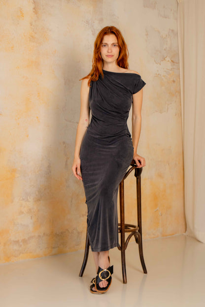 Model wearing Drape Cupro Midi Dress in Slate Black on a stool against a textured wall.