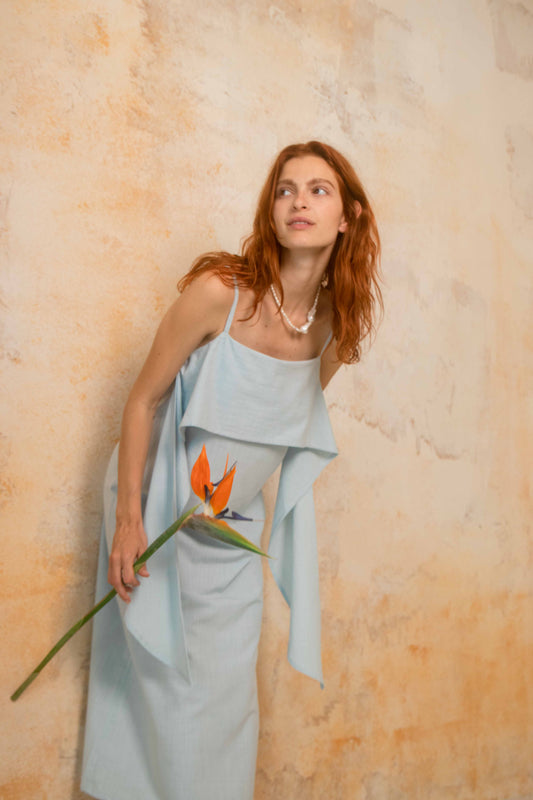 Organic Cotton Sun Dress with Front Frill in Pale Blue worn by a woman holding a flower against a textured background.