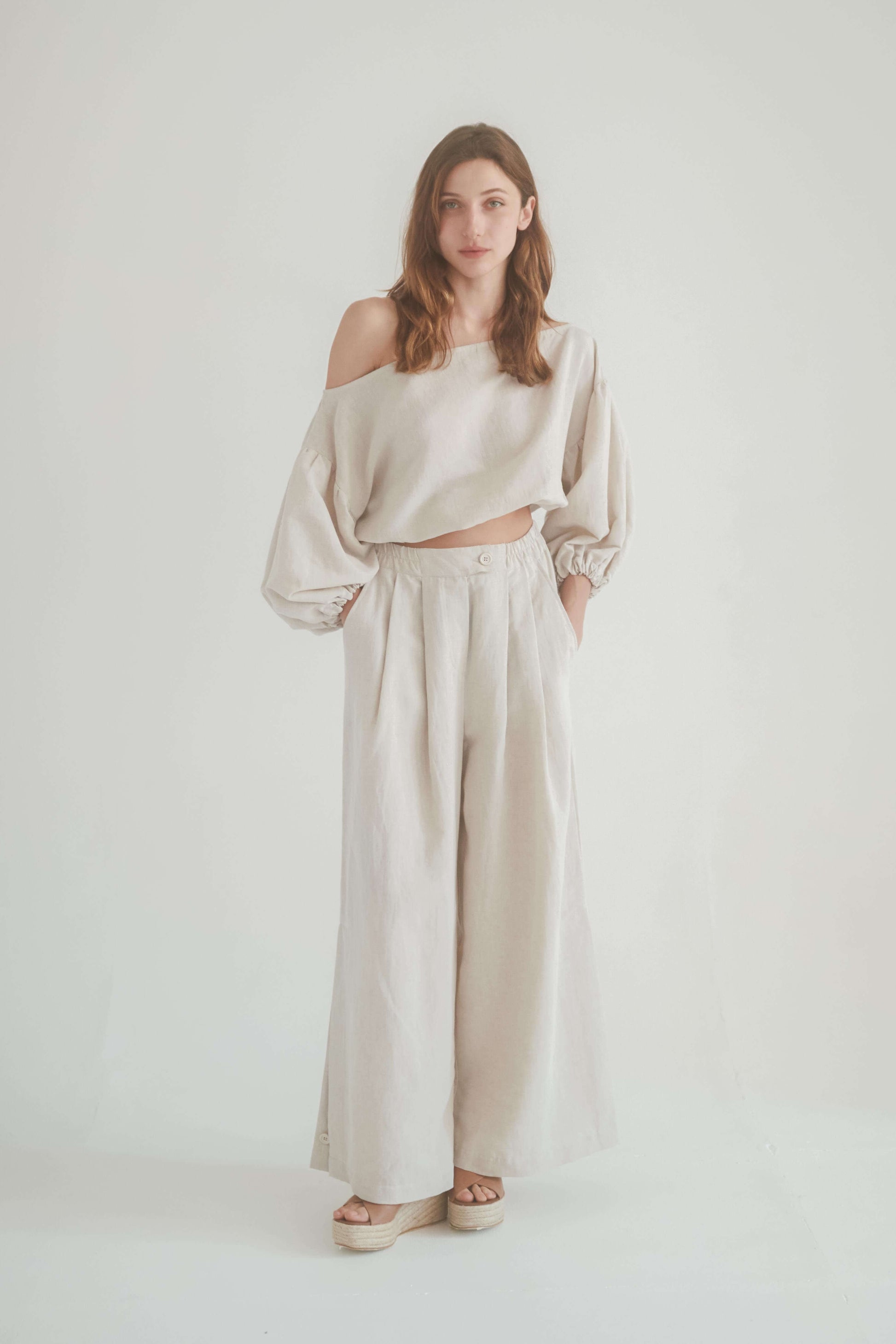 Model wearing a stylish off-shoulder top with wide beige trousers, showcasing a chic and versatile outfit.