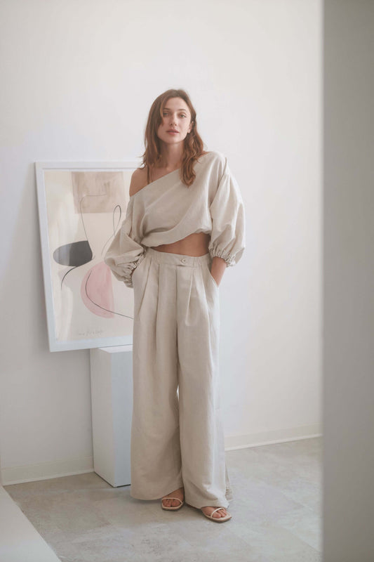 Model wearing natural wide trousers with a cropped top, showcasing a stylish and elegant look in a minimalistic setting.