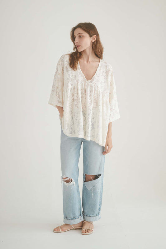 Ecru lace boho tunic top with V-neckline and wide sleeves, styled with ripped denim jeans.