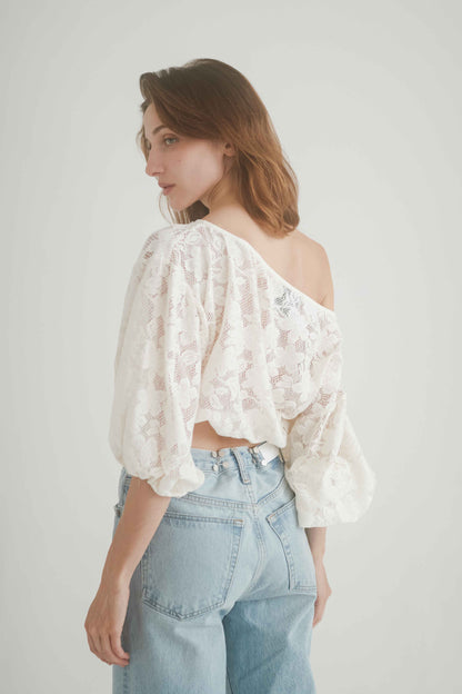 Elegant off-shoulder lace blouse with balloon sleeves and elasticated waist, styled with jeans for a chic look.