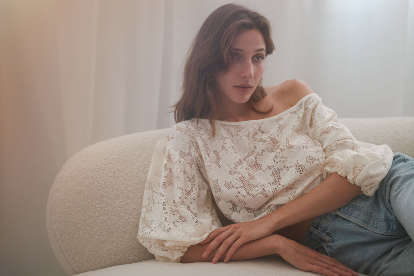 Elegant off-shoulder lace blouse with balloon sleeves, styled with jeans for a chic look.