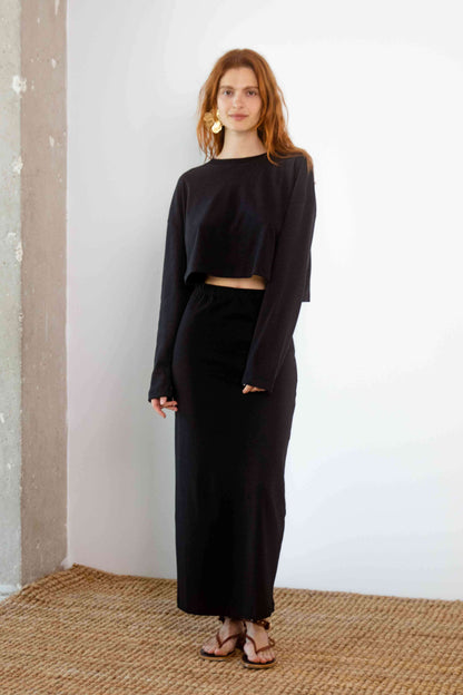 Model wearing Organic Cotton Midi Skirt in Black with a cropped black top, styled for modern spring-summer fashion.