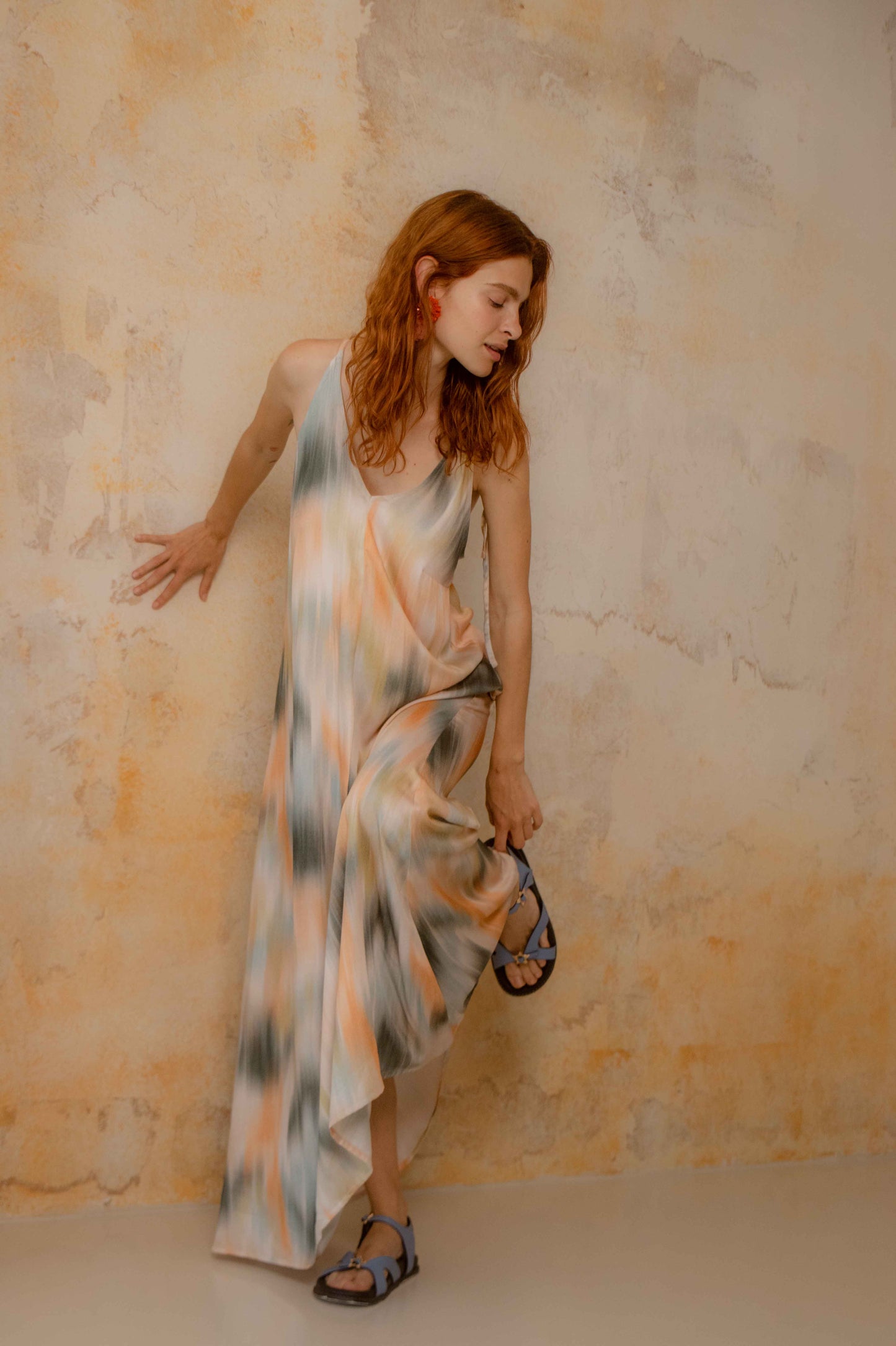 Model wearing a Printed Ecovero Viscose Maxi Dress, showcasing its fluid design and seasonal print against a textured wall.