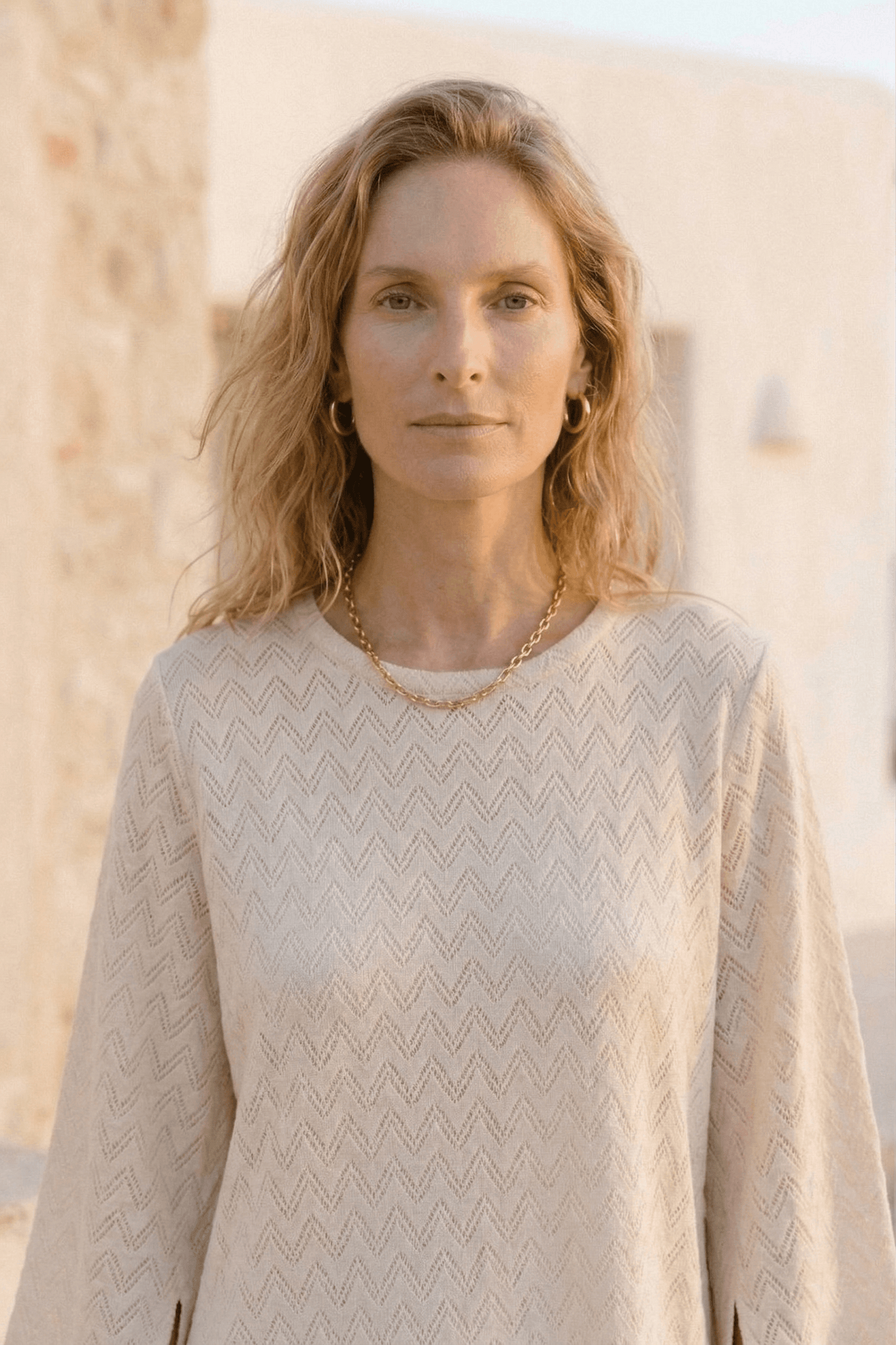 Model wearing an Organic Cotton Crochet Mini Dress, showcasing its airy texture and flared sleeves in ecru color.