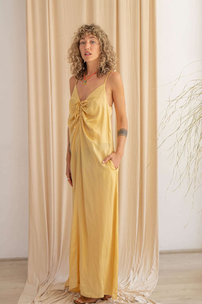 Model wearing a vanilla maxi dress with adjustable straps, showcasing a stylish knot design and pockets.