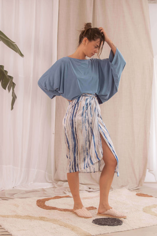 Model showcasing a PRINT WRAP SKIRT in blue and white print, paired with a loose top, on a decorative rug.