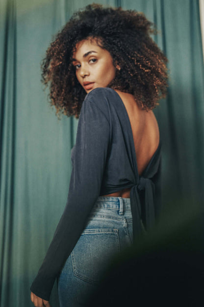 Woman wearing a Cupro Multiway Wrap Top in Slate Black, showcasing back design and styled with high-waisted jeans.