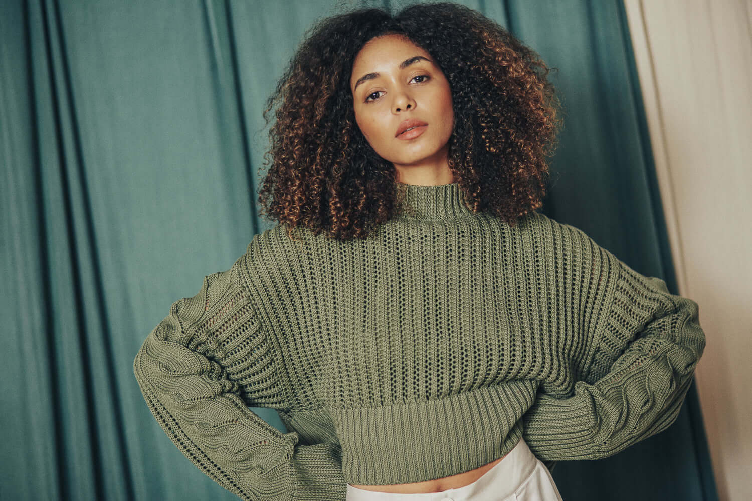 Model wearing a sage green sweater made from 100% organic cotton yarn in Porto, Portugal, showing crop and wide fit