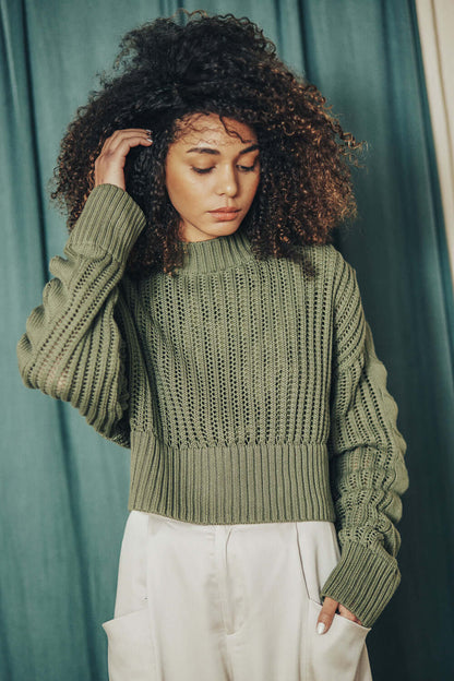 Woman wearing a sage green organic cotton sweater with crop and wide fit, model is 172cm and wears size M.